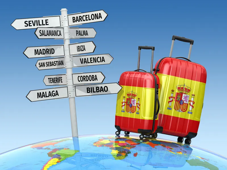 Luggage with Spanish flag beside signpost to top cities in Spain on a globe