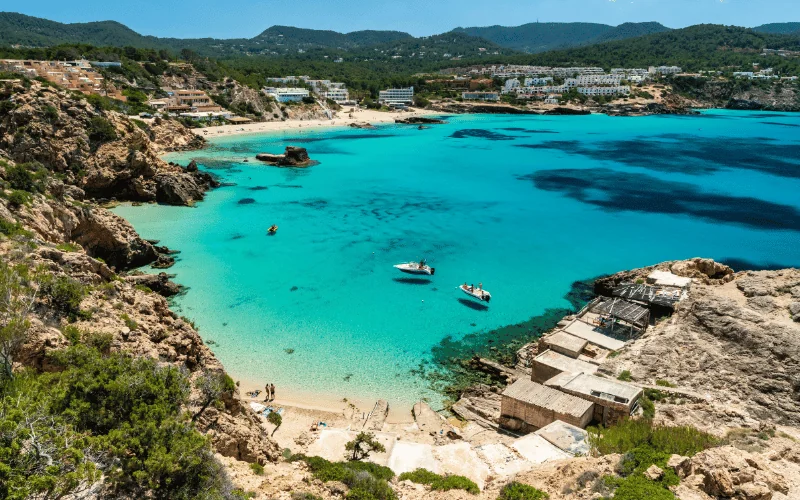 Scenic beach in Ibiza with turquoise waters, boats, and rugged coastline in Spain