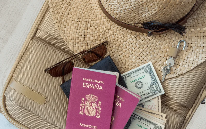 Spanish passports with sunglasses, cash and travel accessories on suitcase