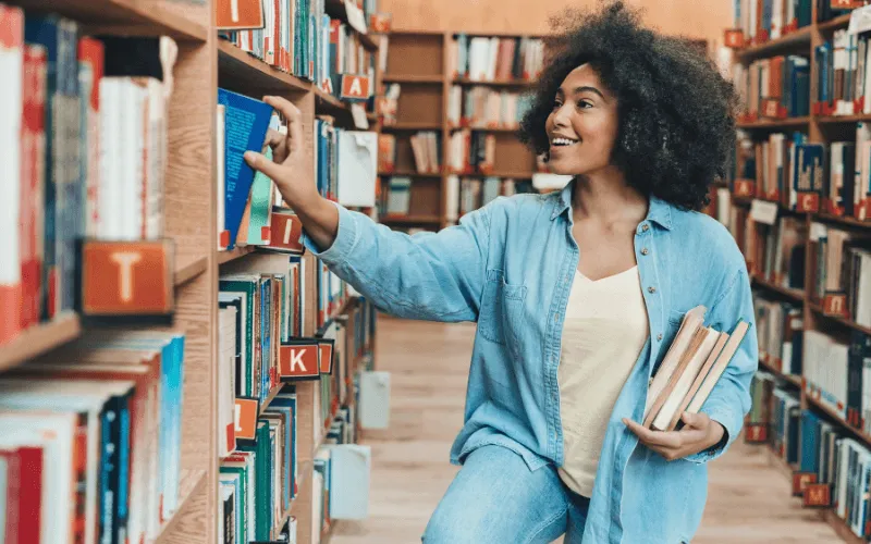 Smiling student choosing a book in a university library in Spain