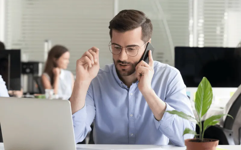 Man talking on phone while working on laptop in modern office