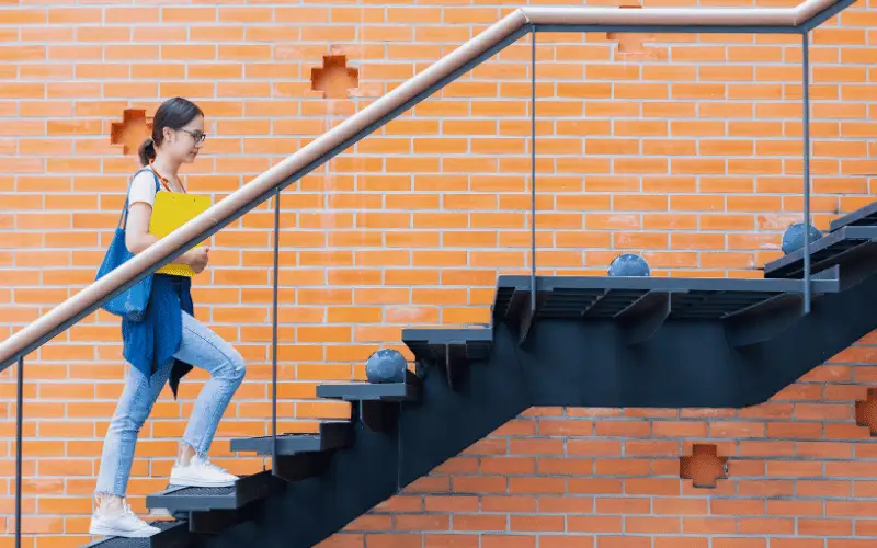 Young student walking up a staircase outside a school building with books in hand