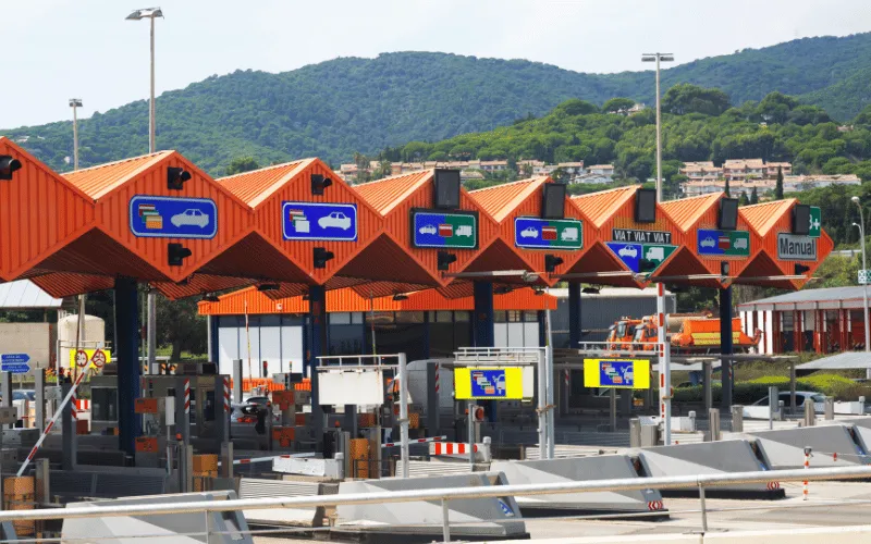 Toll booths on Spanish highway with lanes for cars and trucks against mountain backdrop