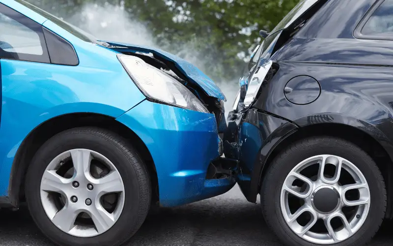 Front end collision between two cars on a road showing damage to both vehicles after an accident