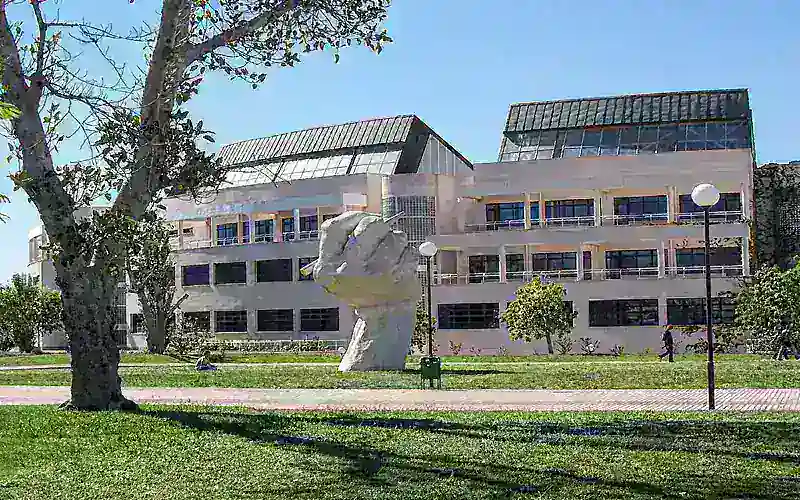 University of Alicante building with sculpture on green campus under blue sky