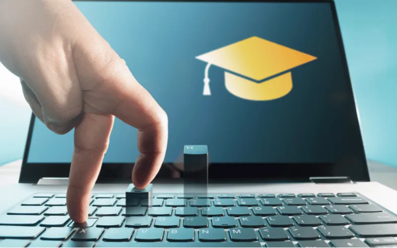 Online learning concept with fingers on keyboard and graduation cap on laptop screen