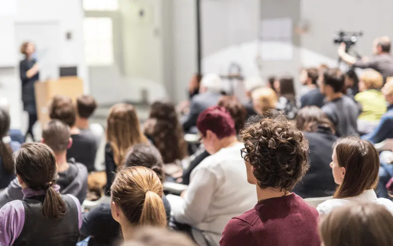 Students attending a university lecture with speaker presenting at front of classroom