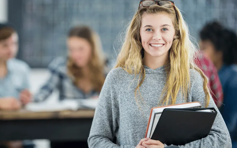 Smiling university student holding books on campus