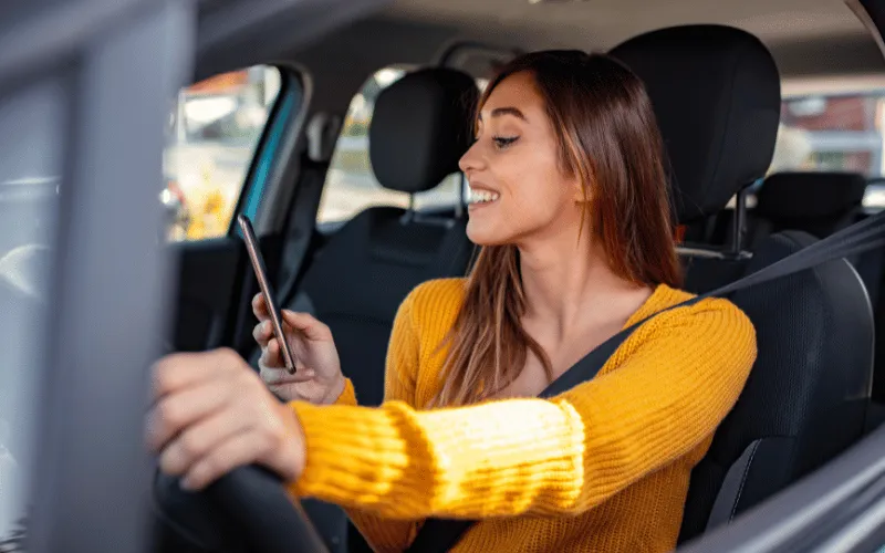 Young woman smiling while using phone behind the wheel of a car