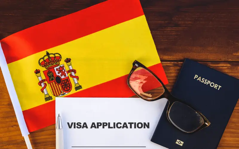 Passport, sunglass, Spanish flag and visa application form on desk