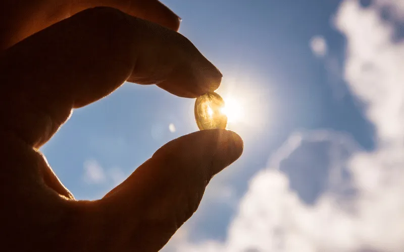 Hand holding vitamin D capsule in sunlight against a blue sky