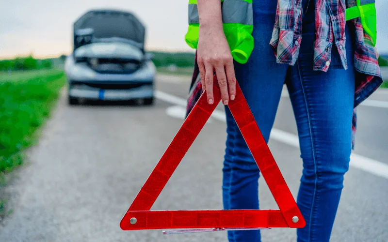 Driver holding warning triangle on roadside near broken down car in Spain