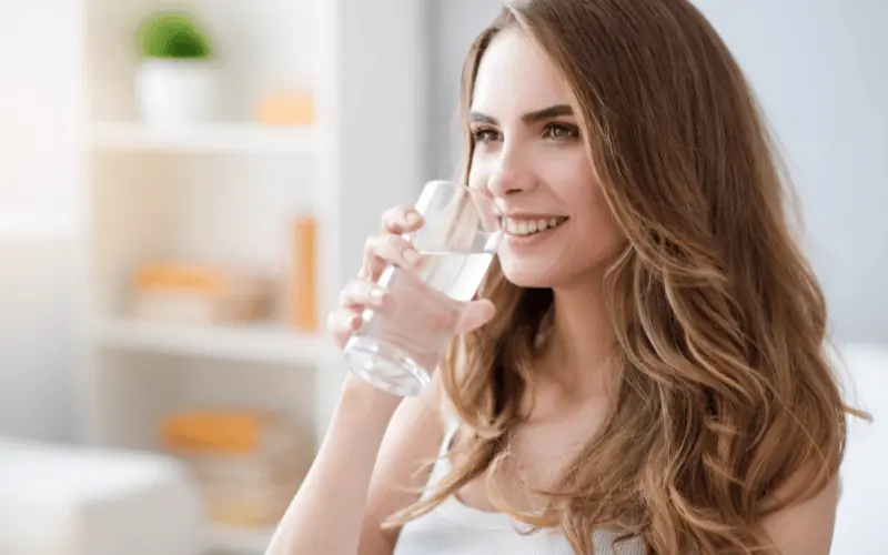 Smiling woman drinking water for hydration and healthy lifestyle at home
