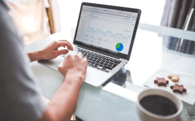 Man analysing website traffic data on laptop with coffee and snacks at home workspace