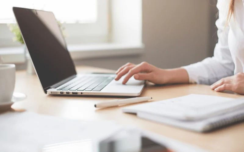 Professional working remotely on laptop at desk with notebook and coffee